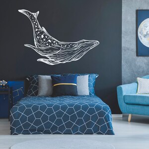 May include: A blue bed with a geometric patterned duvet cover and white pillows. The headboard is against a dark blue wall with a white whale silhouette decal. A blue armchair with a white pillow is in the corner of the room.