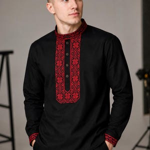 May include: Black long-sleeve shirt with red floral embroidery on the collar, front, and cuffs. The shirt has a mandarin collar and a button-down front. The embroidery features a detailed geometric pattern. The shirt is paired with black pants.