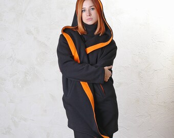 Op de afbeelding: Een zwarte hoodie met oranje bies. De jas heeft een lange, vloeiende snit en wordt gedragen over een zwarte broek.