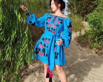 May include: A bright blue off-the-shoulder dress featuring long, voluminous sleeves and a matching tie-waist belt. The garment is decorated with black and pink floral embroidery patterns across the chest, sleeves, and skirt, finished with long tassels.