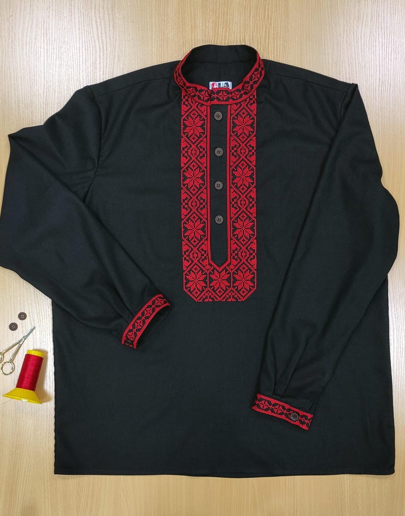 May include: Black long-sleeve shirt with red embroidered floral patterns on the collar, front, and cuffs. The shirt has a mandarin collar and buttoned cuffs. Sewing supplies, including scissors, thread, and buttons, are visible.