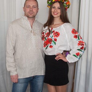 May include: A beige long-sleeved shirt with white embroidery and a white long-sleeved shirt with red and green floral embroidery, paired with a black skirt and a colorful floral crown featuring autumn-toned leaves and flowers.