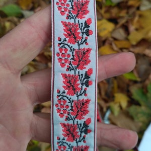 Puede incluir: Cinta blanca con un patrón floral rojo y negro. El patrón presenta flores y hojas estilizadas.
