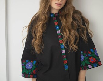 May include: A black button-up shirt with colorful embroidered flowers on the sleeves and down the front. The shirt has a high collar and a relaxed fit.
