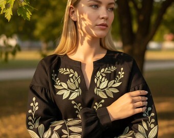 May include: Black long-sleeve blouse with a V-neck and leaf embroidery in shades of green and gold. The blouse features a relaxed fit with gathered sleeves. The embroidery is concentrated around the neckline and on the sleeves.