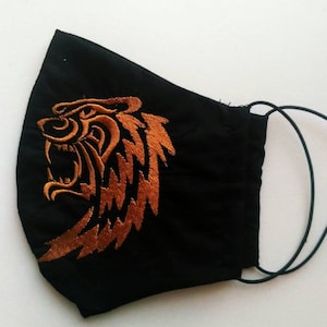 Puede incluir: Máscara facial negra con un diseño de cabeza de tigre naranja bordado.