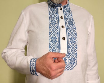 Peut inclure: Une chemise blanche à manches longues avec un motif brodé bleu sur le devant. La chemise a un col montant et une fermeture boutonnée.