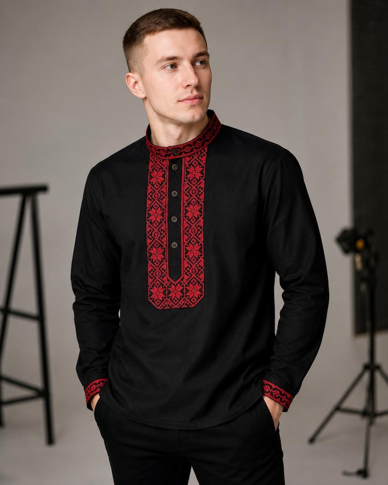 May include: Black long-sleeve shirt with red floral embroidery on the collar, front, and cuffs. The shirt has a mandarin collar and a button-down front. The embroidery features a detailed geometric pattern. The shirt is paired with black pants.