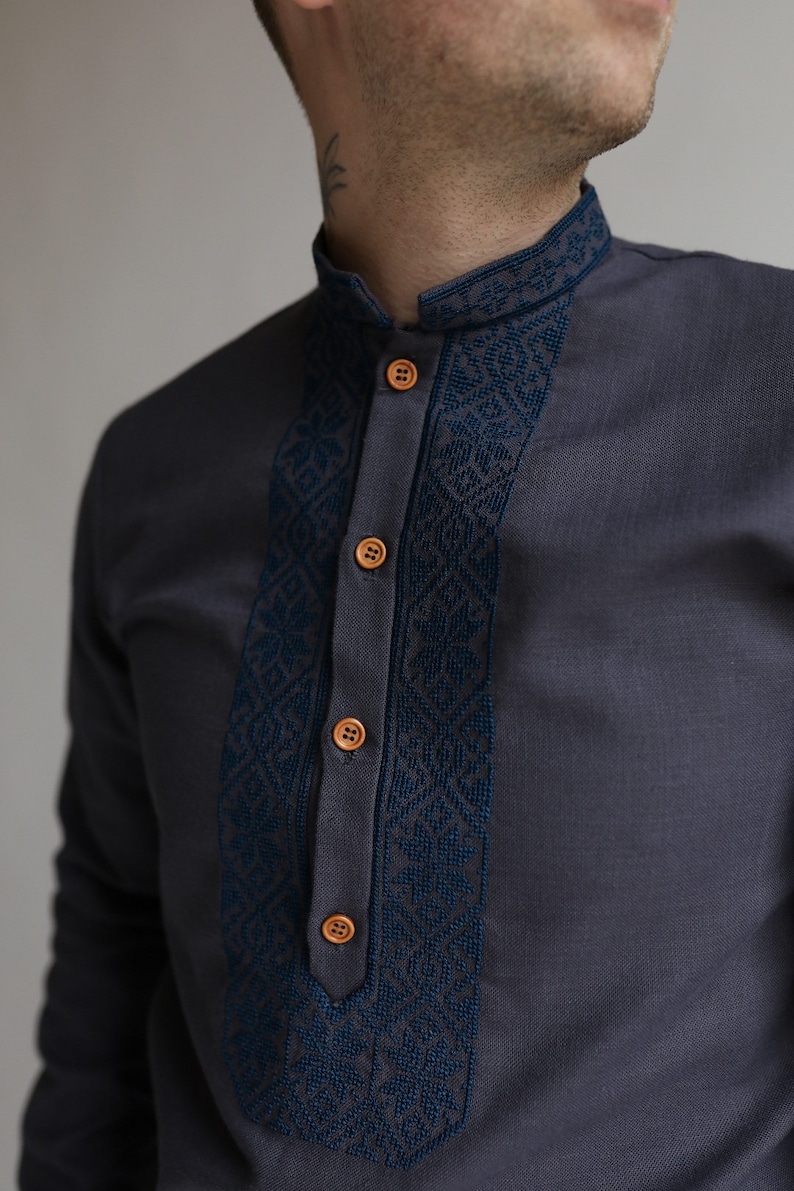 May include: Charcoal gray shirt with a mandarin collar and a decorative navy blue embroidered panel down the front. The shirt features wooden buttons and a detailed geometric pattern on the collar and panel.