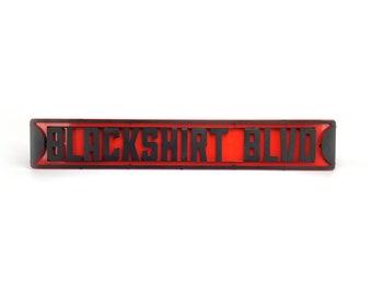 May include: A red street sign with black lettering that reads "BLACKSHIRT BLVD".