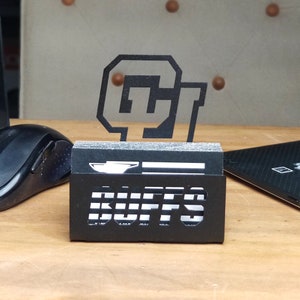 May include: Black metal business card holder with a cutout of the University of Colorado Buffaloes logo and the word "BUFFS".