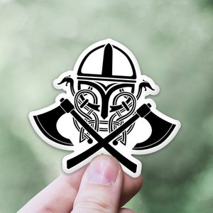 May include: Black and white sticker of a Viking helmet with two crossed axes. The helmet is decorated with intricate knotwork.