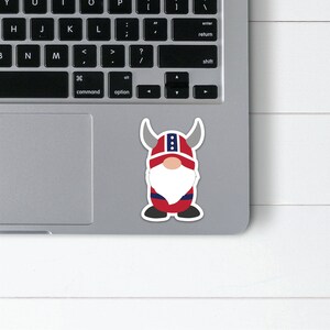 K&ouml;nnte beinhalten: Ein roter und blauer Zwerg mit einem geh&ouml;rnten Helm mit wei&szlig;en Verzierungen. Der Zwerg hat einen wei&szlig;en Bart und steht auf einem grauen Laptop.