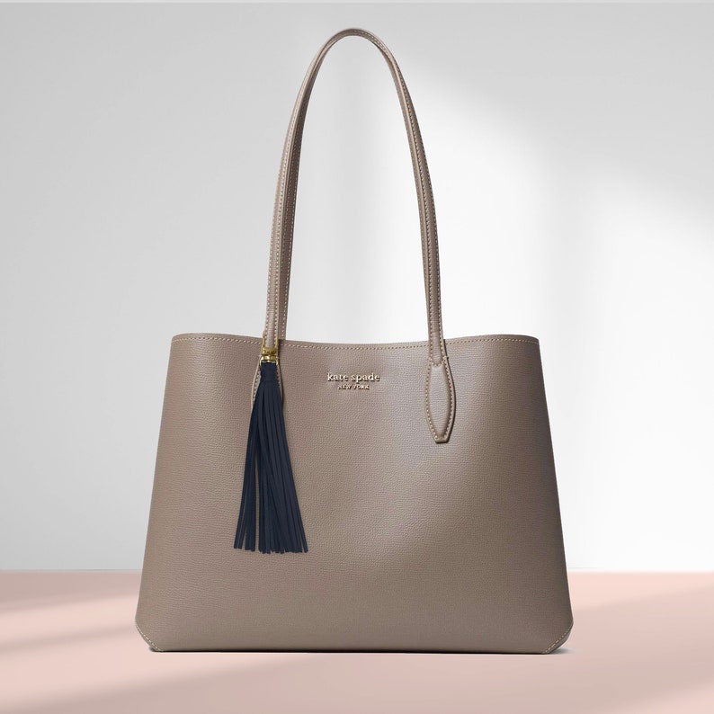 May include: A light brown leather tote bag with a black tassel. The bag has a gold zipper and the brand name "kate spade new york" is printed on the front.