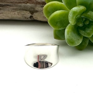 May include: A silver ring with a smooth, rounded, and slightly curved top. The ring is made of polished metal and has a reflective surface.