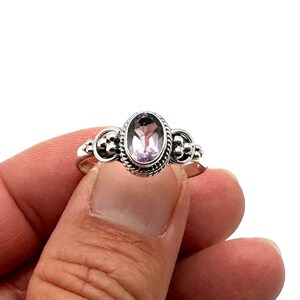 May include: A silver ring with an oval-shaped amethyst gemstone set in a decorative bezel. The ring has a beaded design on the band.
