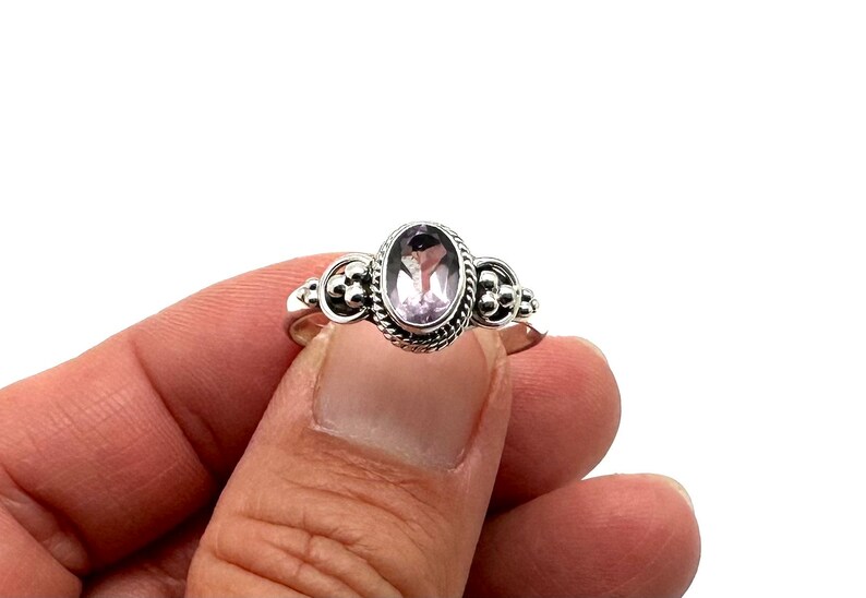 May include: A silver ring with an oval-shaped amethyst gemstone set in a decorative bezel. The ring has a beaded design on the band.