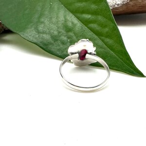May include: A silver ring with a red gemstone set in a floral design.