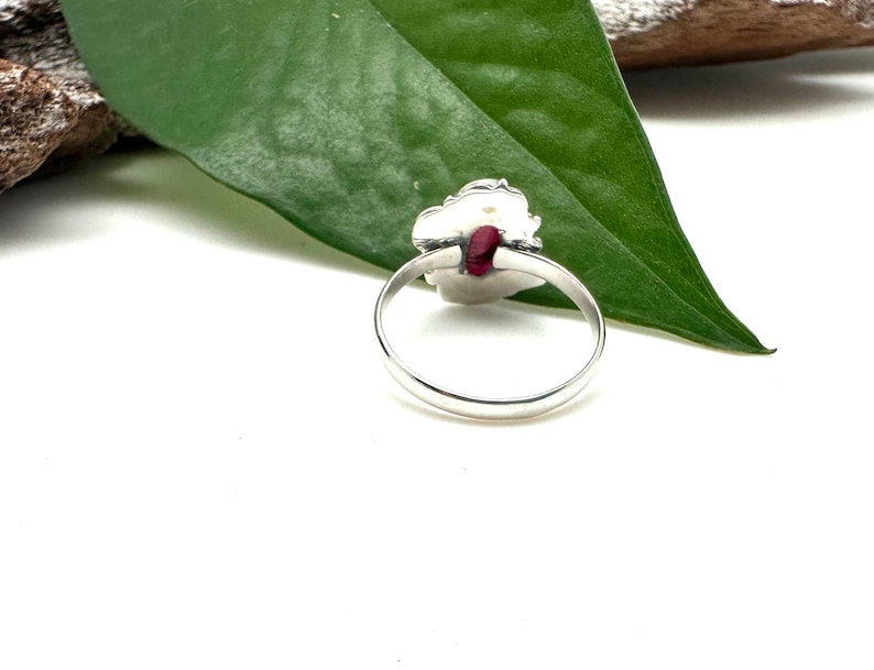May include: A silver ring with a red gemstone set in a floral design.
