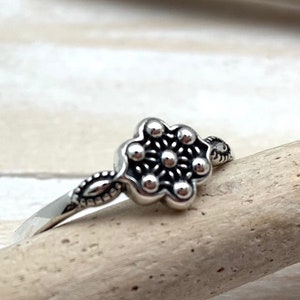 May include: A silver ring featuring a flower-shaped design. The flower has a textured centre with small raised dots and a smooth outer edge.