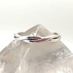 May include: A silver braided ring on a white crystal surface.