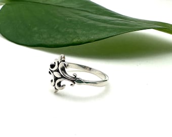 May include: A silver ring featuring a decorative, ornate design. The ring is made from sterling silver and has a delicate, intricate pattern.