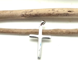 May include: A polished silver-toned metal cross pendant featuring a smooth, reflective surface and rounded edges. The cross has a simple, clean design with a small integrated bail at the top for attachment to a chain or cord, showcasing a bright finish.