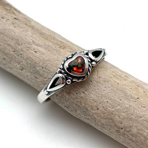 May include: A silver ring with a heart-shaped opal gemstone. The ring has a delicate design with small details around the stone.