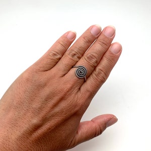 May include: A silver ring with a spiral design. The ring is on a person's finger.
