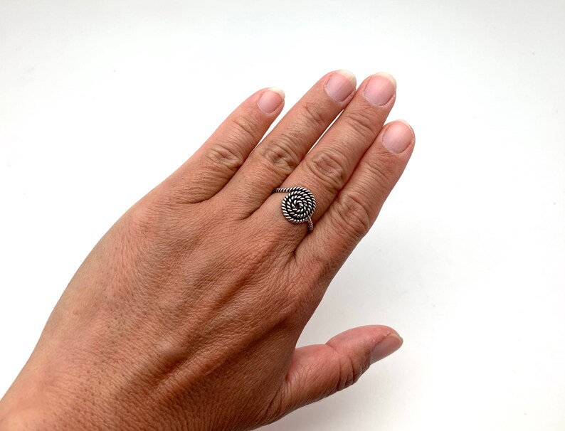 May include: A silver ring with a spiral design. The ring is on a person's finger.