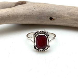 Op de afbeelding: Een zilveren ring met een rode edelsteen in een geperde zetting.