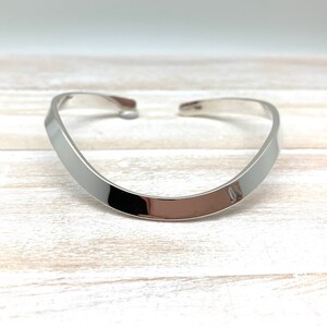May include: A silver, curved bangle bracelet with a smooth, polished finish.