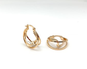 May include: A pair of gold hoop earrings with a double-layered design. The earrings are made of a thin, delicate metal and have a simple, elegant style.