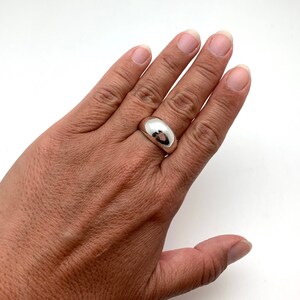May include: A silver dome ring with a smooth, polished finish. The ring is worn on the middle finger of a hand.