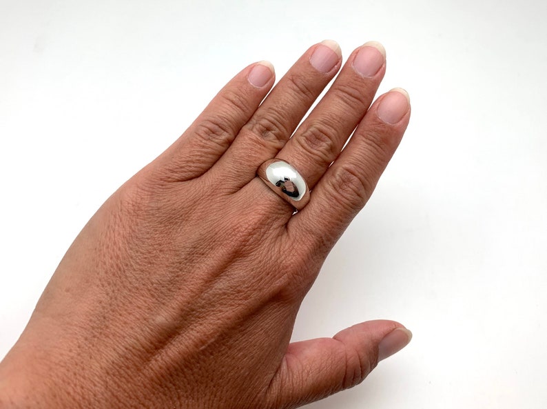 May include: A silver dome ring with a smooth, polished finish. The ring is worn on the middle finger of a hand.