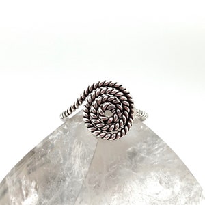 May include: Silver ring with a twisted, spiral design. The ring is made of a single piece of wire that is twisted into a circle.