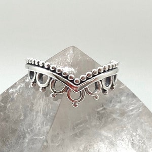 Puede incluir: Un anillo de plata con un delicado diseño en forma de V, con un borde de cuentas y recortes intrincados.