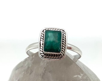 Puede incluir: Un anillo de plata con una piedra preciosa verde cuadrada engastada en un borde decorativo.
