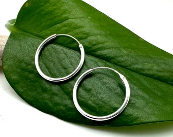 May include: A pair of silver hoop earrings on a green leaf. The earrings are simple and classic, with a smooth, polished finish.