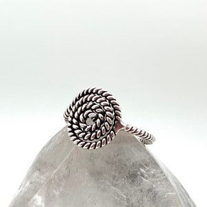 May include: A silver ring with a spiral design. The ring is made of twisted wire and has a circular shape.