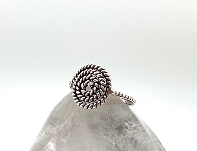 May include: A silver ring with a spiral design. The ring is made of twisted wire and has a circular shape.