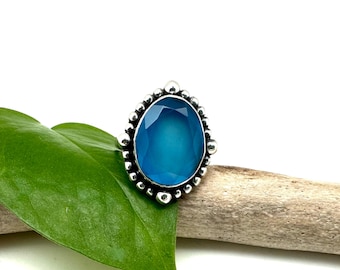 May include: A silver ring with a large, oval-shaped blue gemstone set in a beaded bezel.