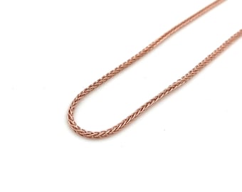 May include: Rose gold wheat chain necklace. The chain has a warm, metallic colour and features a woven design. The necklace is displayed against a white background, highlighting its intricate texture and colour.