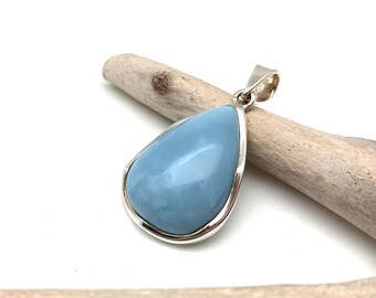 May include: A teardrop-shaped blue opal pendant set in a silver bezel. The pendant is resting on a piece of driftwood.