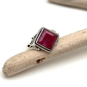 May include: A silver ring with a square-shaped ruby gemstone set in a decorative silver frame.