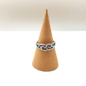 Puede incluir: Un anillo de plata con un diseño de espiral, mostrado en un soporte de anillo de madera.