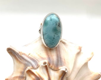 Op de afbeelding: Een zilveren ring met een lichtblauwe ovale edelsteen. De edelsteen heeft een marmerpatroon.