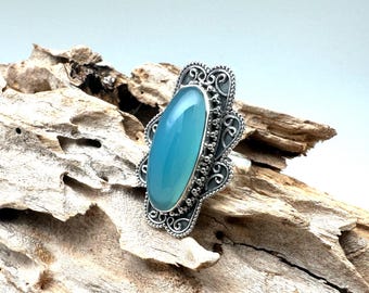 May include: A silver ring with a large, oval-shaped, light blue gemstone set in a filigree design.