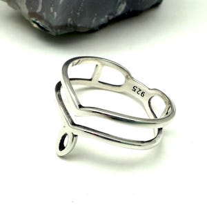 May include: A sterling silver ring with a unique open design. The ring features a double band with a heart-shaped top and a stylized teardrop detail. The ring is stamped with "925".