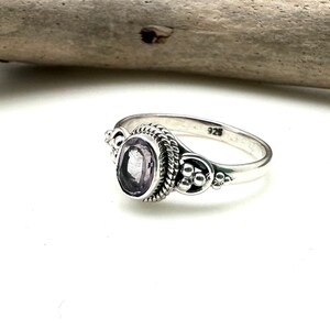 May include: A silver ring with a purple gemstone set in a decorative bezel. The ring has a twisted band and is marked "925" on the inside.